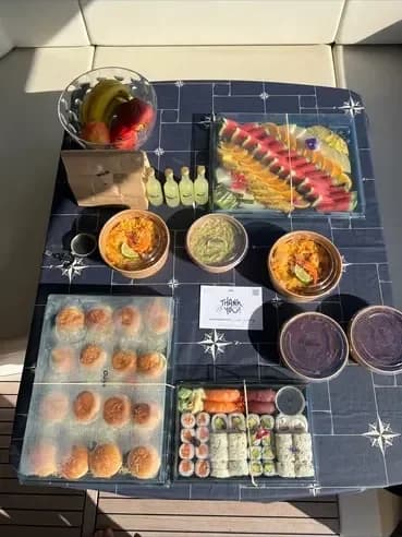 Boxed meals, sushi, fruit and drinks set out on a table on a yacht deck