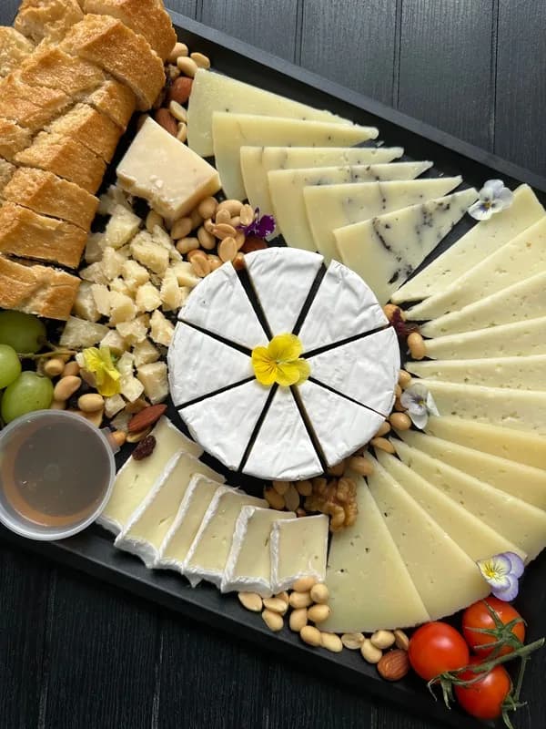 A cheese board fanned with sliced cheeses, bread, nuts and cherry tomatoes
